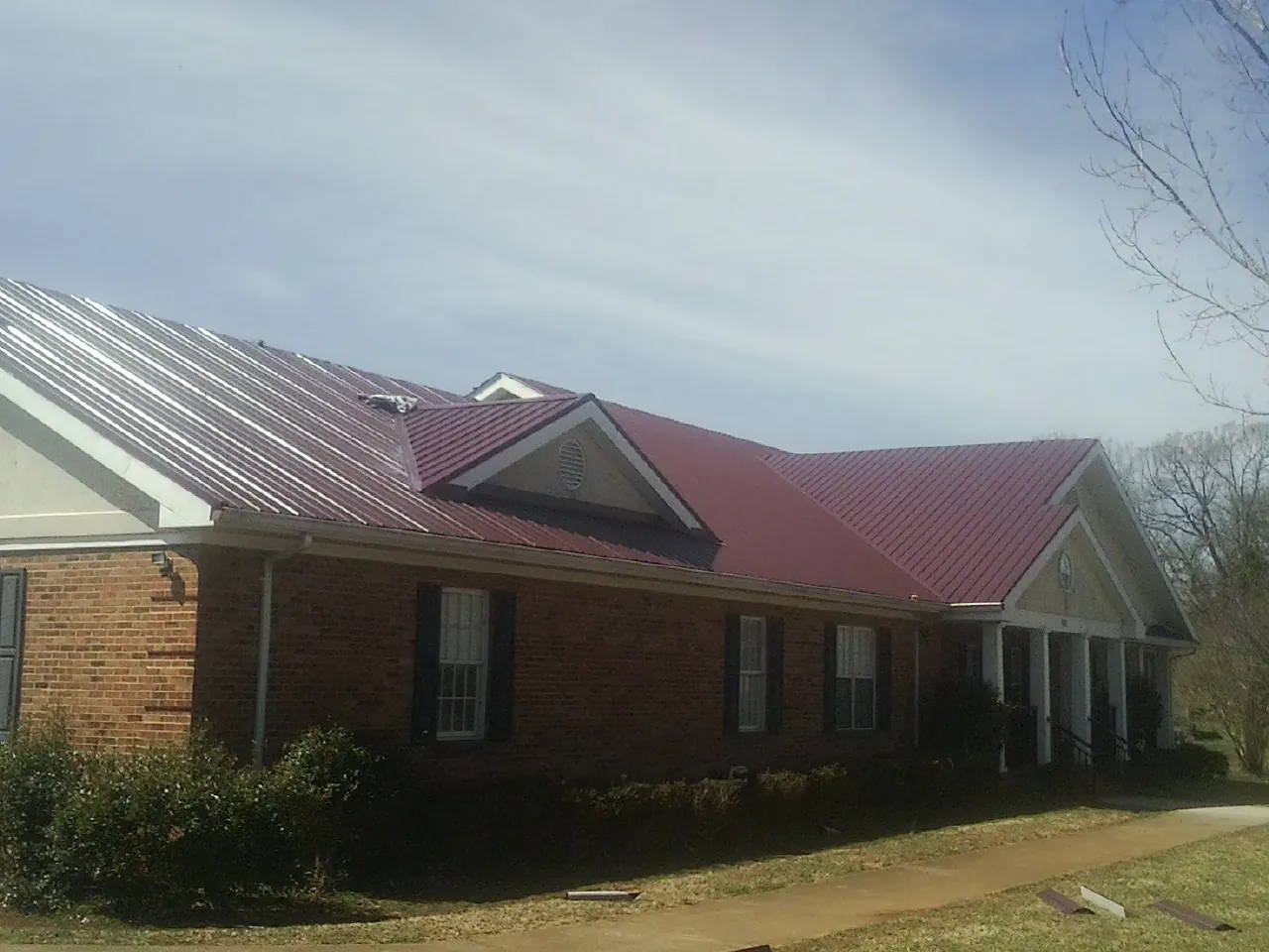 Red metal roof with gabled entries on a long brick building, from a Hail Damage Roof Repair job in Tallapoosa