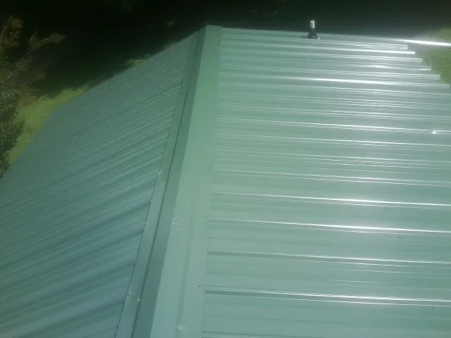 New green metal panels meeting at the ridge of a roof — Flat Roof Repair work by our crew in Tallapoosa