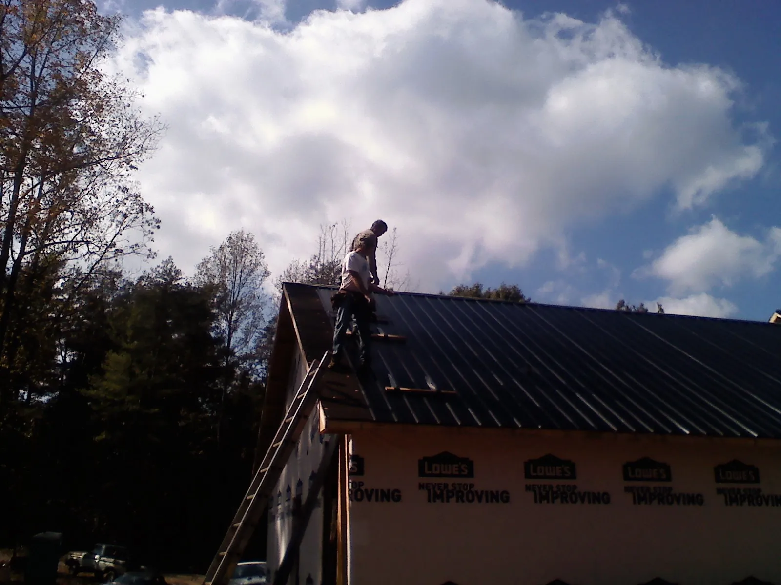 Roofer fastening dark metal panels high against a cloudy sky, from a Roof Inspection job in Tallapoosa