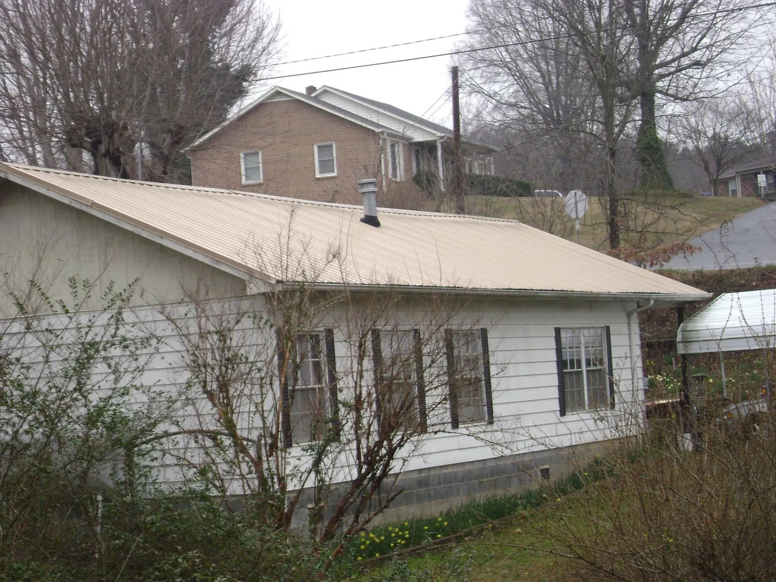 Tan metal roof on a white sided house set into a hillside — Commercial Roofing by Roofing Brothers in Tallapoosa