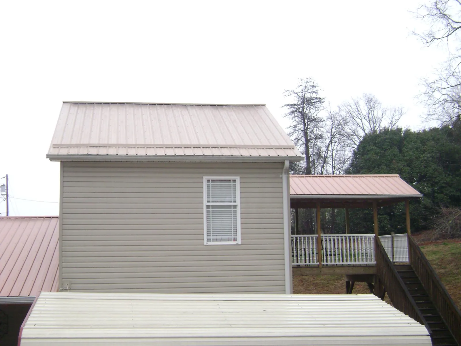 Tan metal roofs on a two story addition and attached porch, from a Roof Replacement job in Tallapoosa